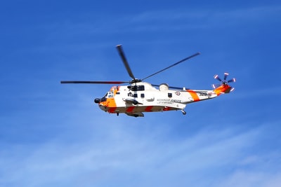 橙色和白色的直升机白天在蓝天下飞行